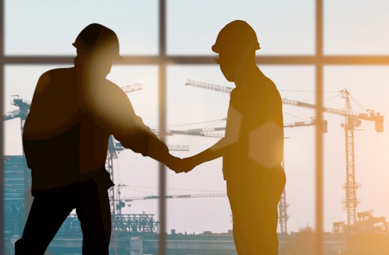 two men shaking hands with large construction in the background